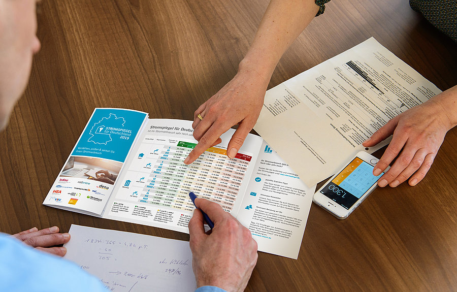 auf einem tisch liegt eine rechnung und ein taschenrechner, drei Hände sind zu sehen