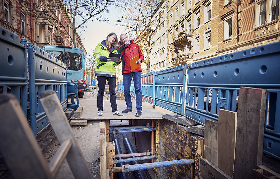 Mann und Frau stehen am Rande einer Fernwärmebaustelle und beraten sich.