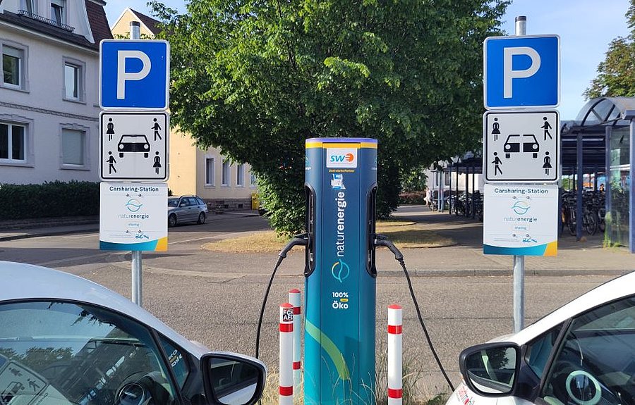 E-Ladesäule mit zwei ladenden Fahrzeugen und Verkehrsschildern